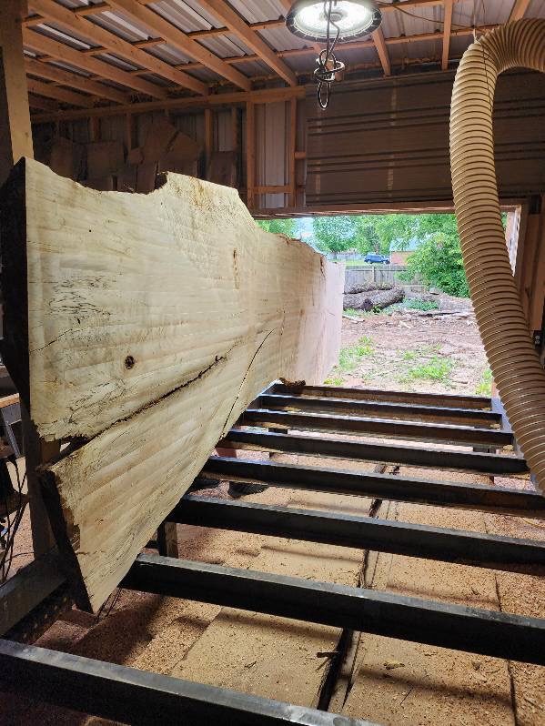 A wide pale slab stood on edge on the steel flattening table with a dust hose overhead.