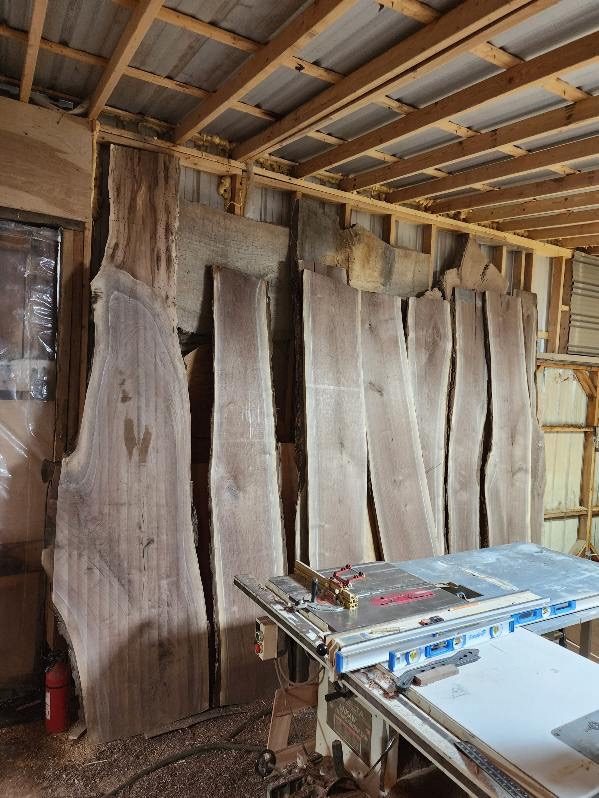 Rough sawn slabs stood on edge along the barn wall to dry, a jointer in the foreground.